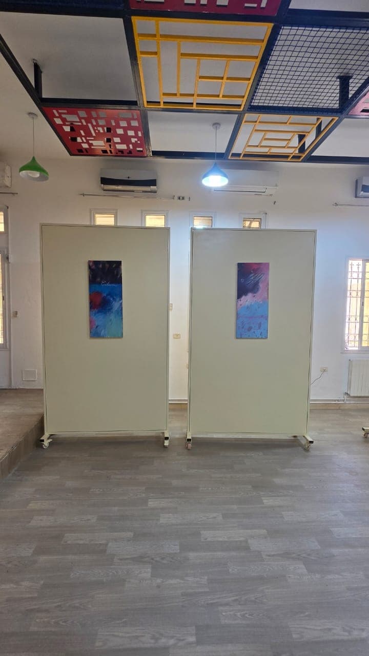 Deux cimaises mobiles présentant chacune une peinture abstraite bleue et rouge, sous le faux plafond coloré.